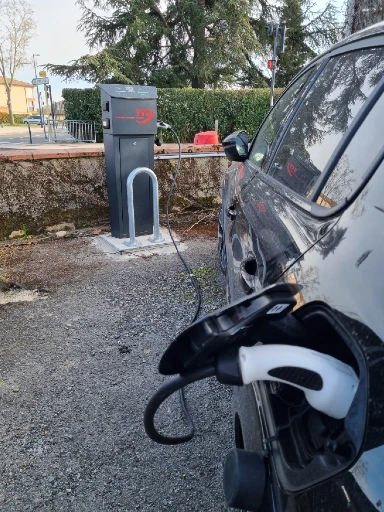 une station de recharge de marque scame en plein chargement d'une voiture noire sur un parking d'entreprise
